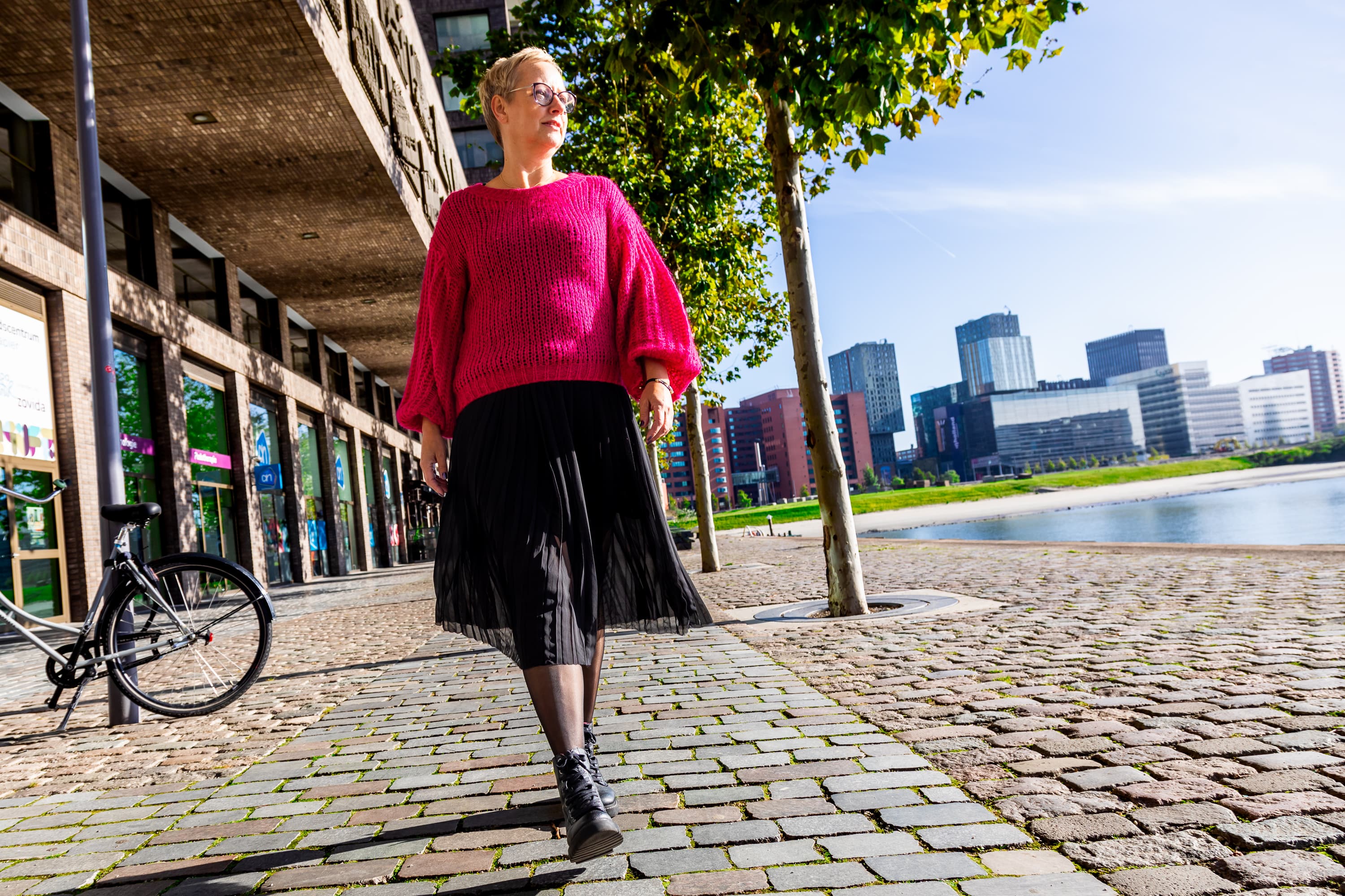 Joke van der Kraan, grafisch vormgever en eigenaar van VormBuilders, gefotografeerd in het stedelijke landschap van Rotterdam, waar haar professionele uitstraling en warme persoonlijkheid vastgelegd zijn tegen een achtergrond van dynamische architectuur.